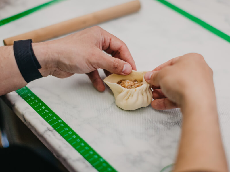 Close up of hands pinching dough to wrap up the filling and form a dumpling